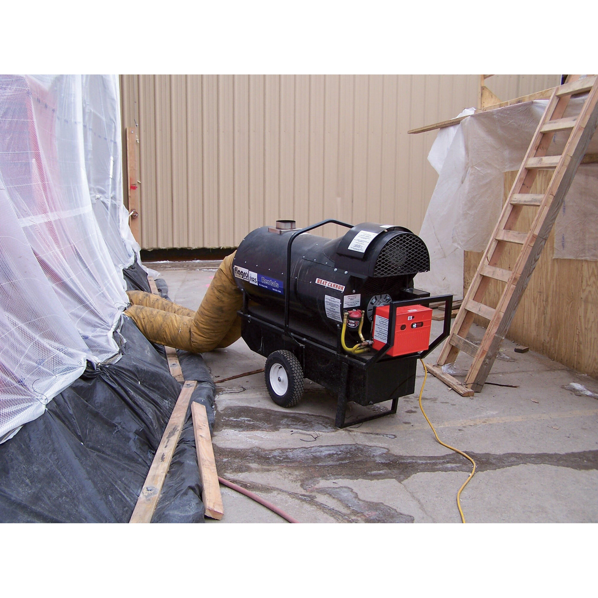 Mobile forced-air heater unit connected by a flexible yellow duct into a temporary plastic-sheet enclosure on a construction site.